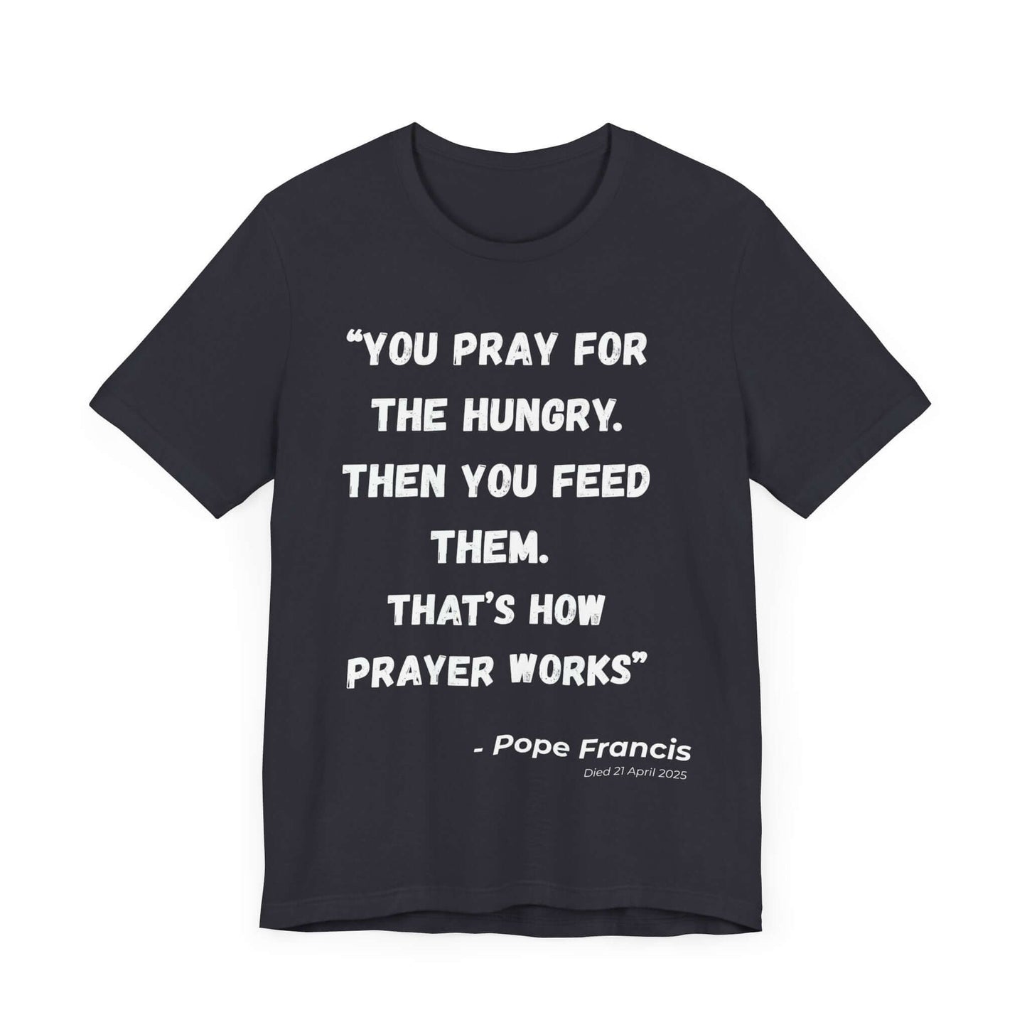 Dark grey t-shirt featuring the quote “You pray for the hungry. Then you feed them. That’s how prayer works.” in bold white lettering, with attribution to Pope Francis and his date of passing. A minimal Catholic tribute shirt for fans of faith-driven justice.