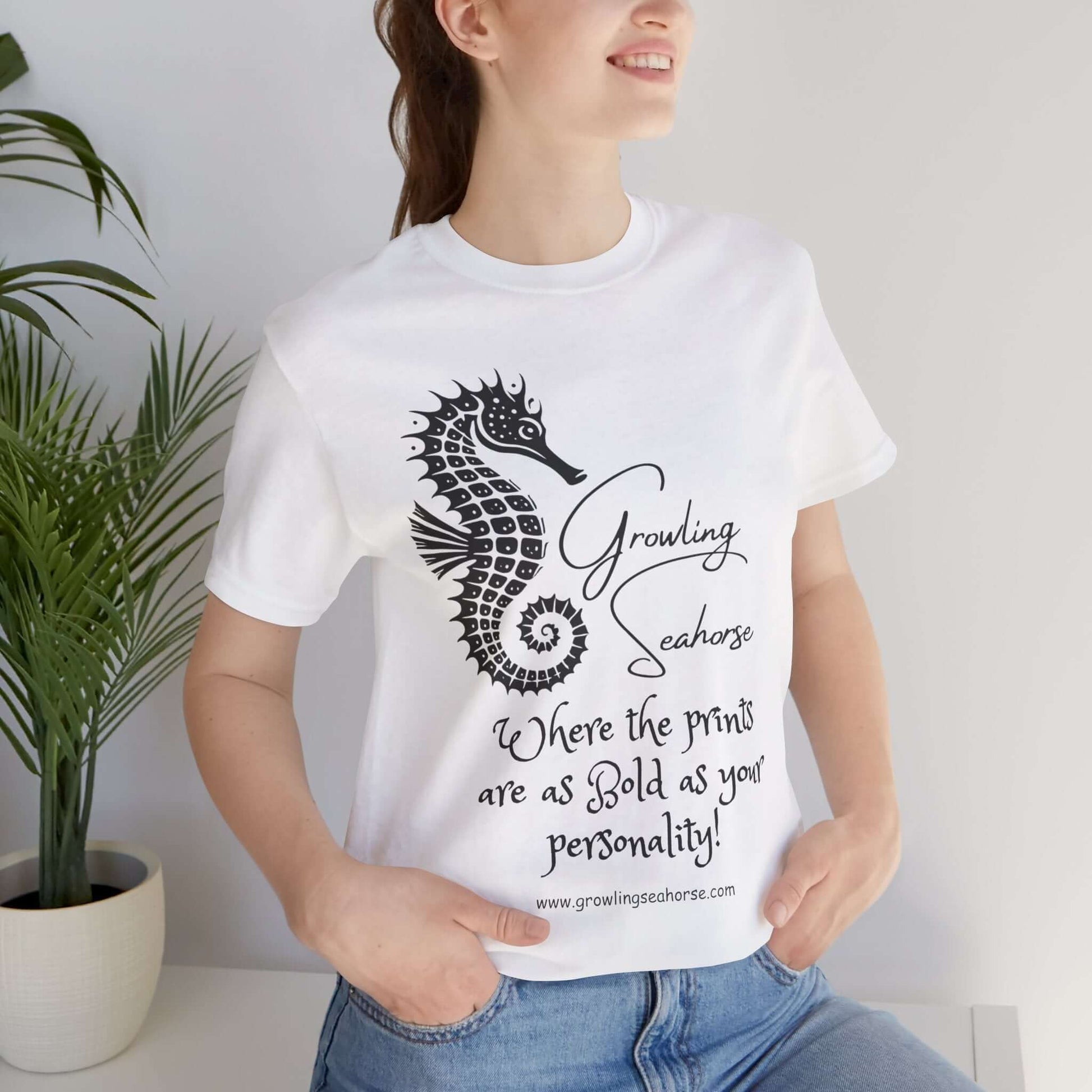 Woman wearing a white unisex t-shirt featuring the Growling Seahorse brand mascot, Gus—a bold black stylized seahorse with a spiral tail. Below the seahorse, the script reads “Growling Seahorse” and “Where the prints are as bold as your personality!” Perfect for quirky fashion fans and unapologetic personalities.