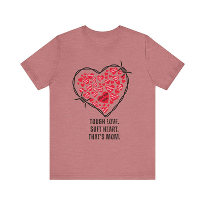 Mauve-colored shirt featuring a barbed wire heart filled with red hearts and mom-centric notes, paired with the phrase “Tough Love. Soft Heart. That’s Mom.” A fierce, funny tribute in soft tones.
