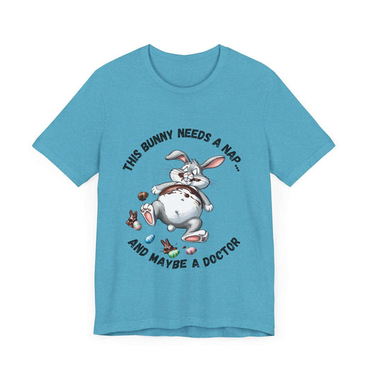 Lite Blue t-shirt showcasing a humorous graphic of a chubby cartoon bunny flat on its back, clearly in a post-snack meltdown. The bunny is surrounded by chocolate wrappers, smears, and a vacant stare of snack regret. The curved text above and below the illustration reads: “This Bunny Needs a Nap… and Maybe a Doctor.” The playful design pops against the cool blue fabric, making it an ideal funny Easter shirt, casual spring tee, or go-to outfit for anyone who knows the true meaning of chocolate coma.