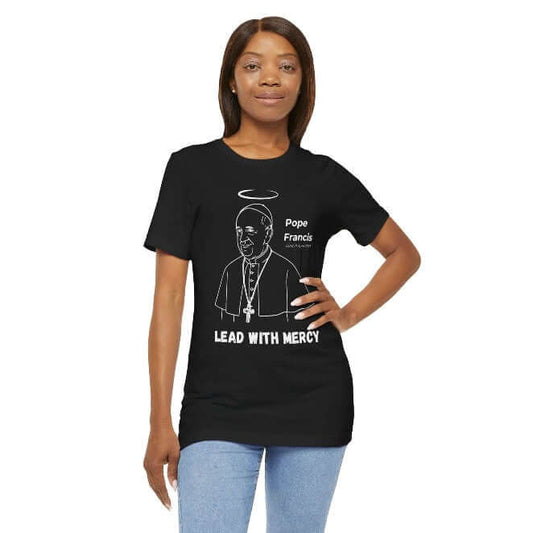 Woman wearing a black t-shirt with minimalist white line art of Pope Francis, halo above his head, and the bold quote “Lead With Mercy.” A spiritual Catholic tribute tee honoring The Humble Pope’s legacy of compassion, humility, and justice.