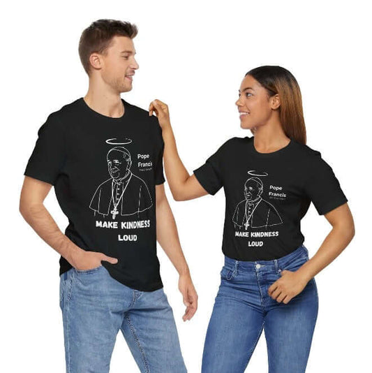 Smiling man and woman wearing black matching t-shirts featuring minimalist white line art of Pope Francis with a halo and the quote “Make Kindness Loud.” A Catholic memorial tee honoring The Humble Pope’s legacy of mercy, justice, and love — perfect for couples, friends, or faithful duos.