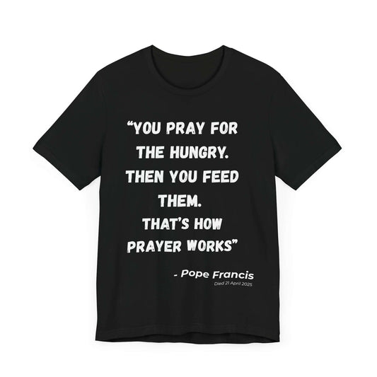 Black t-shirt with a bold white typographic design featuring the quote “You pray for the hungry. Then you feed them. That’s how prayer works.” and attribution to Pope Francis. A meaningful Catholic tribute tee with minimalist style.